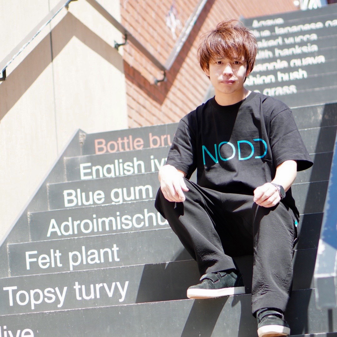 NODDのロゴTシャツで階段に座り胸ロゴが見える石田